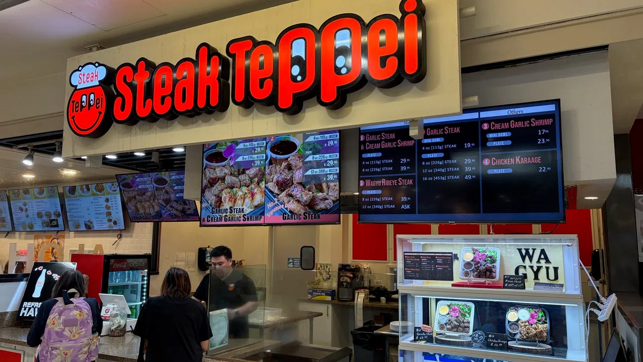 The Steak Teppei counter under a red logo sign, with menu screens listing garlic steak bowls and plates by weight and a lit glass case of sample plates marked Wagyu