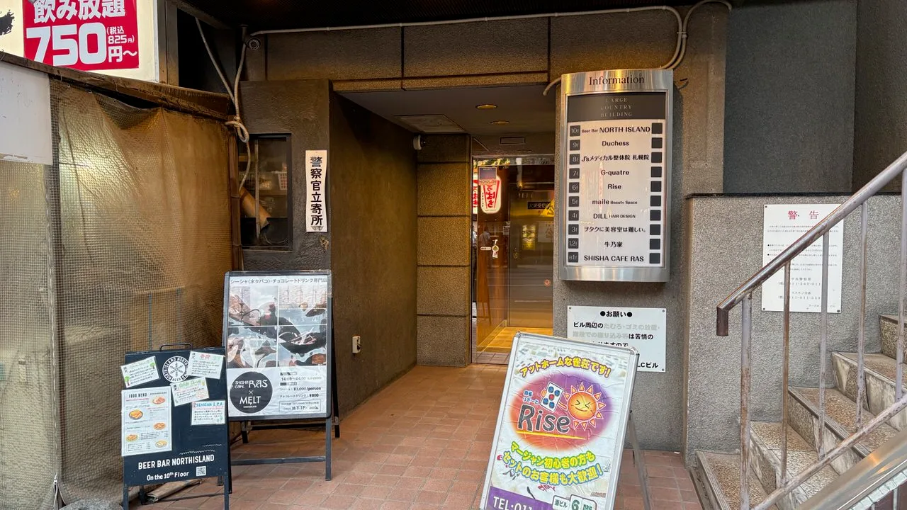 The street-level entrance of a city building with a metal floor-guide board listing tenants and an A-board reading Beer Bar Northisland on the 10th floor
