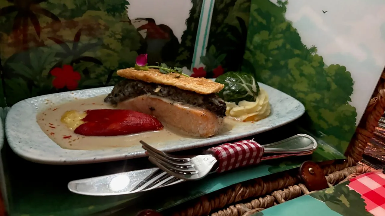 A salmon fillet in pale white wine sauce, topped with something dark and a sheet of pastry, with a stuffed red pepper and mashed potato with a cabbage parcel