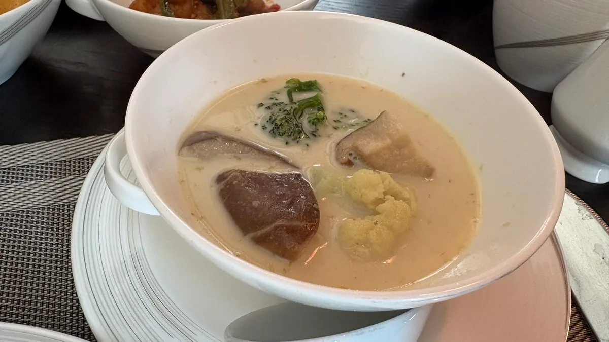 A white bowl of pale green curry with shiitake mushroom, cauliflower and broccoli