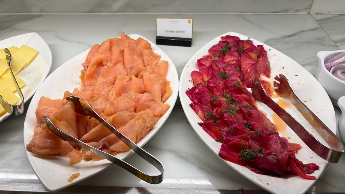 Two white platters of sliced salmon with tongs, one orange and one deep red scattered with dill, behind a card reading Smoked Salmon
