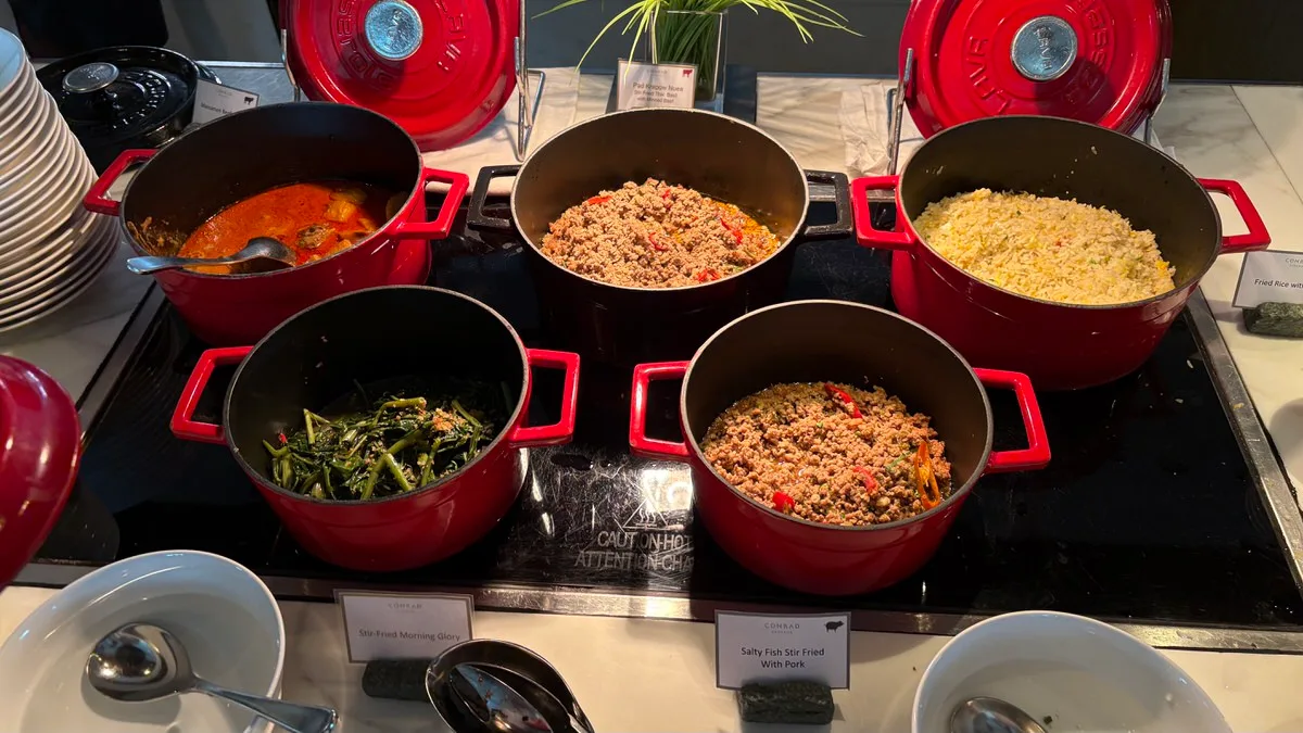Five cast-iron pots on a buffet hot plate, most of them red: an orange-red curry, two pots of minced meat with red chili, fried rice and stir-fried morning glory, with name cards in front