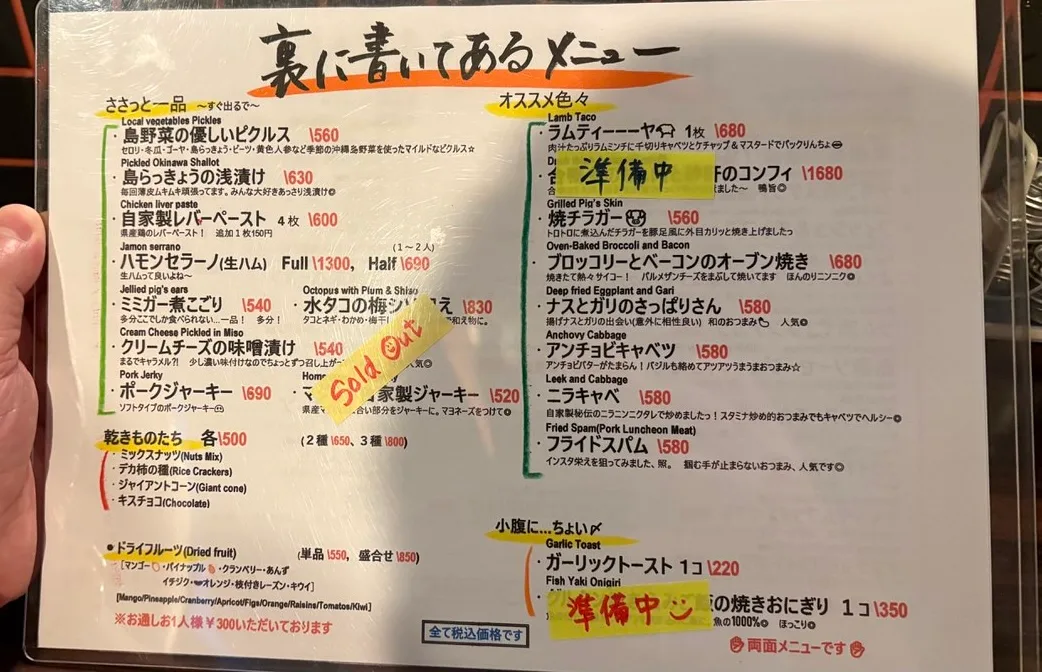 The reverse side of the laminated food menu, headed in Japanese hand lettering, listing small plates and recommendations with English names and prices, three lines covered with sold out and coming soon stickers