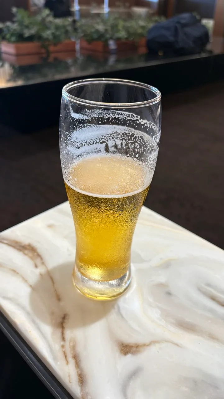 A glass of beer with foam marks above the level, standing on a white marble side table
