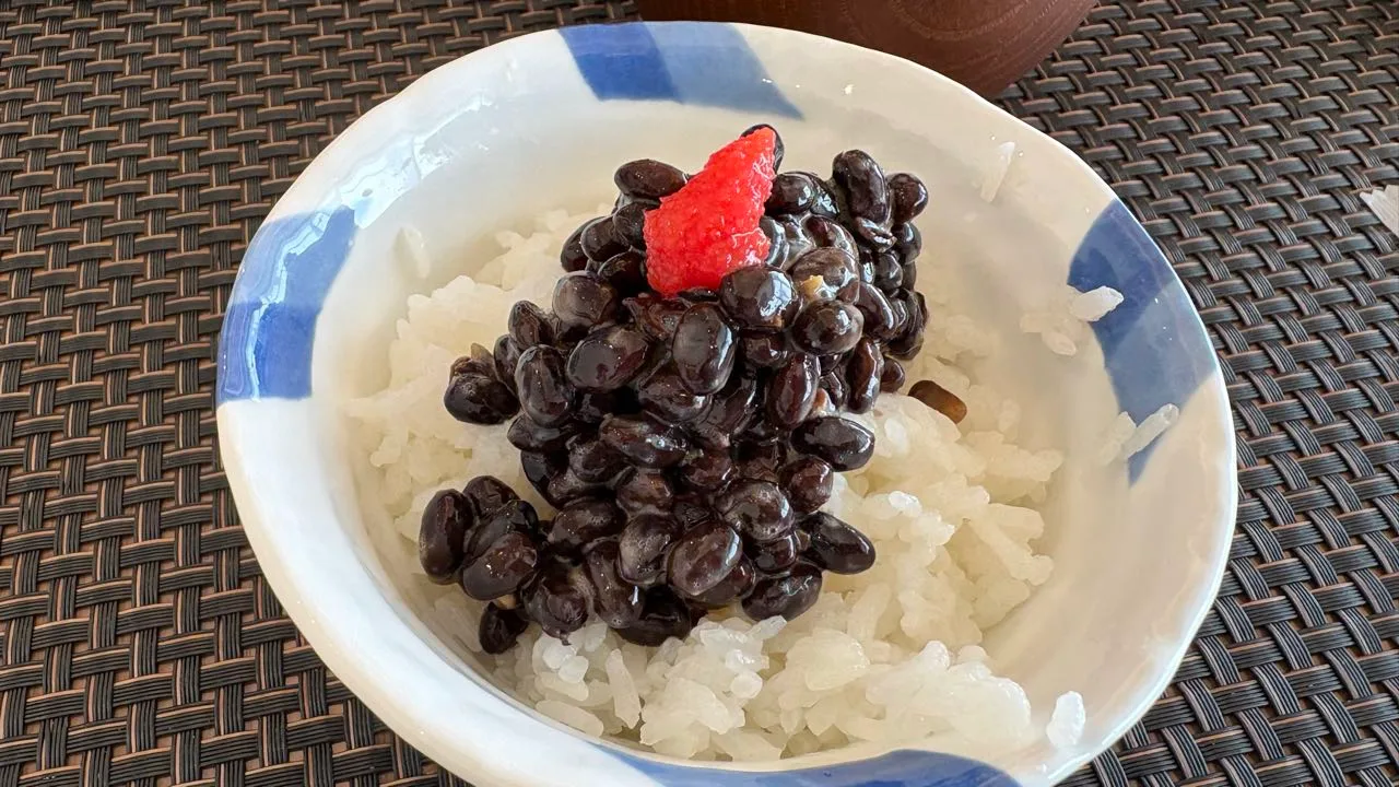 A blue and white bowl of white rice topped with glossy black natto beans and a small piece of pink mentaiko
