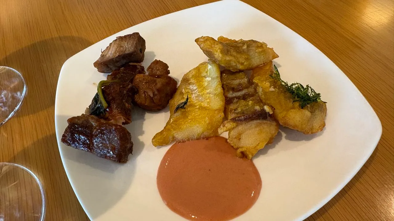 A white plate with chunks of glazed braised pork on the left, pieces of battered white fish topped with dill on the right and a pool of pink sauce in the middle