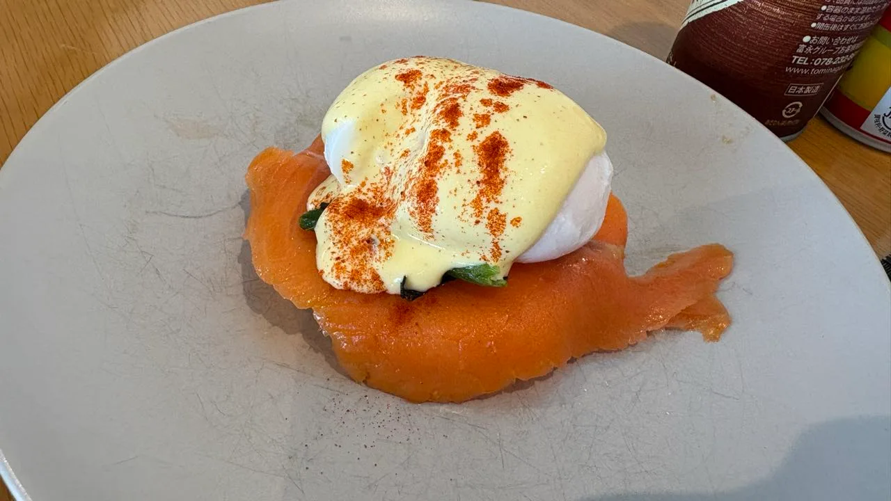 A grey plate holding a poached egg covered in yellow hollandaise dusted with paprika, sitting on a fan of smoked salmon with green leaves underneath
