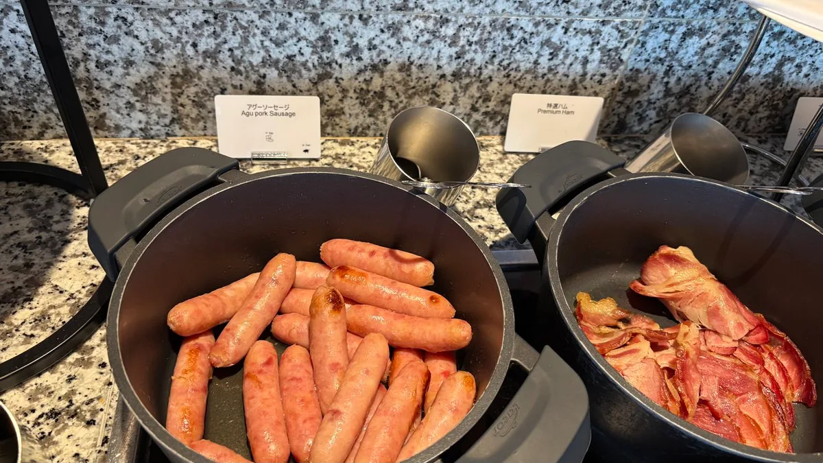 Two buffet pans on a granite counter, one of small sausages labelled Agu pork Sausage and one of sliced ham labelled Premium Ham