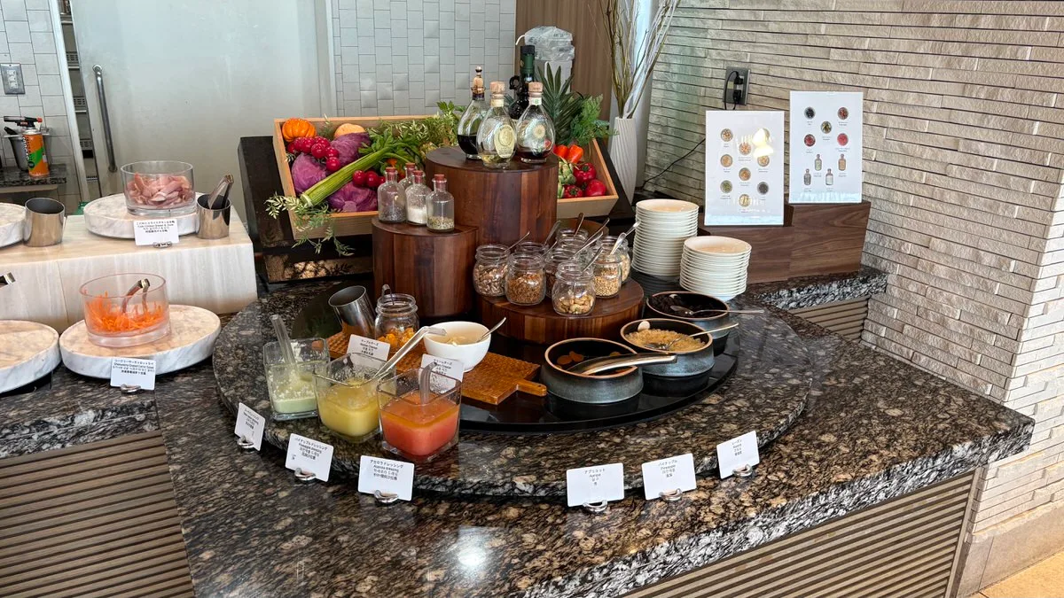 A buffet dressing station with small pitchers of dressing, oil and vinegar bottles, jars of dry toppings and stacks of plates