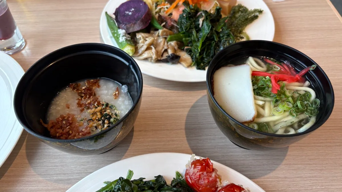 A bowl of rice porridge with crisp fried topping beside a bowl of Okinawa soba with kamaboko, spring onion and pickled red ginger