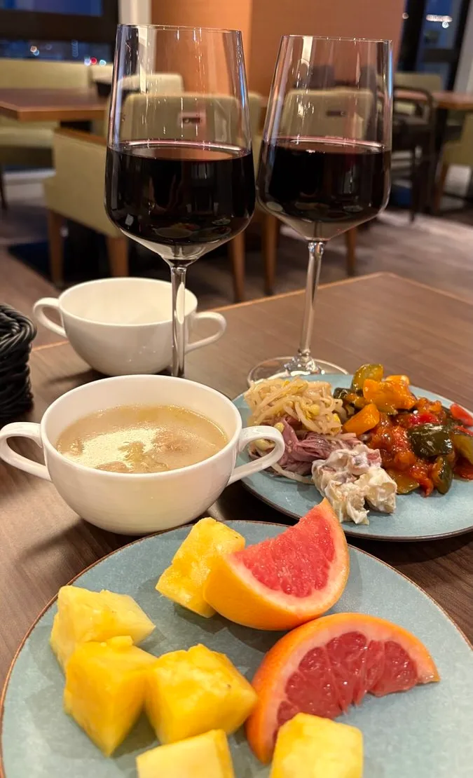 Two glasses of red wine, a soup cup and a plate of vegetables left over from an empty fried chicken tray