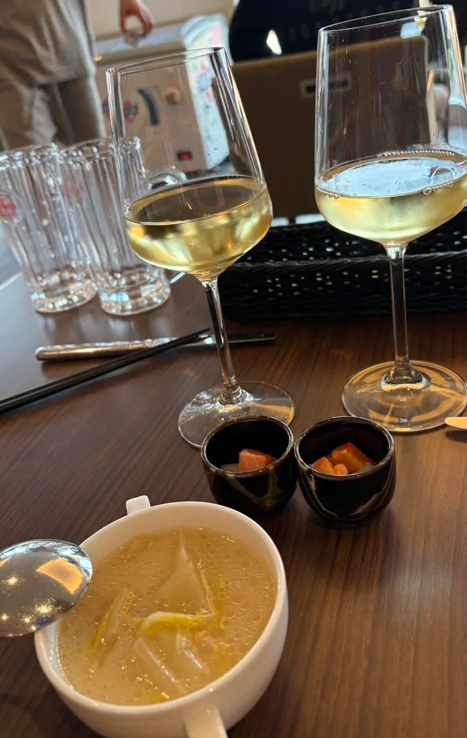 Two glasses of white wine with a bowl of cream soup and two small cups on a lounge table