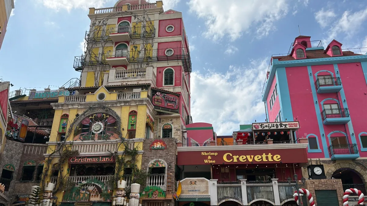 Brightly painted buildings in American Village with signs for Christmas Land and a shrimp and wine restaurant
