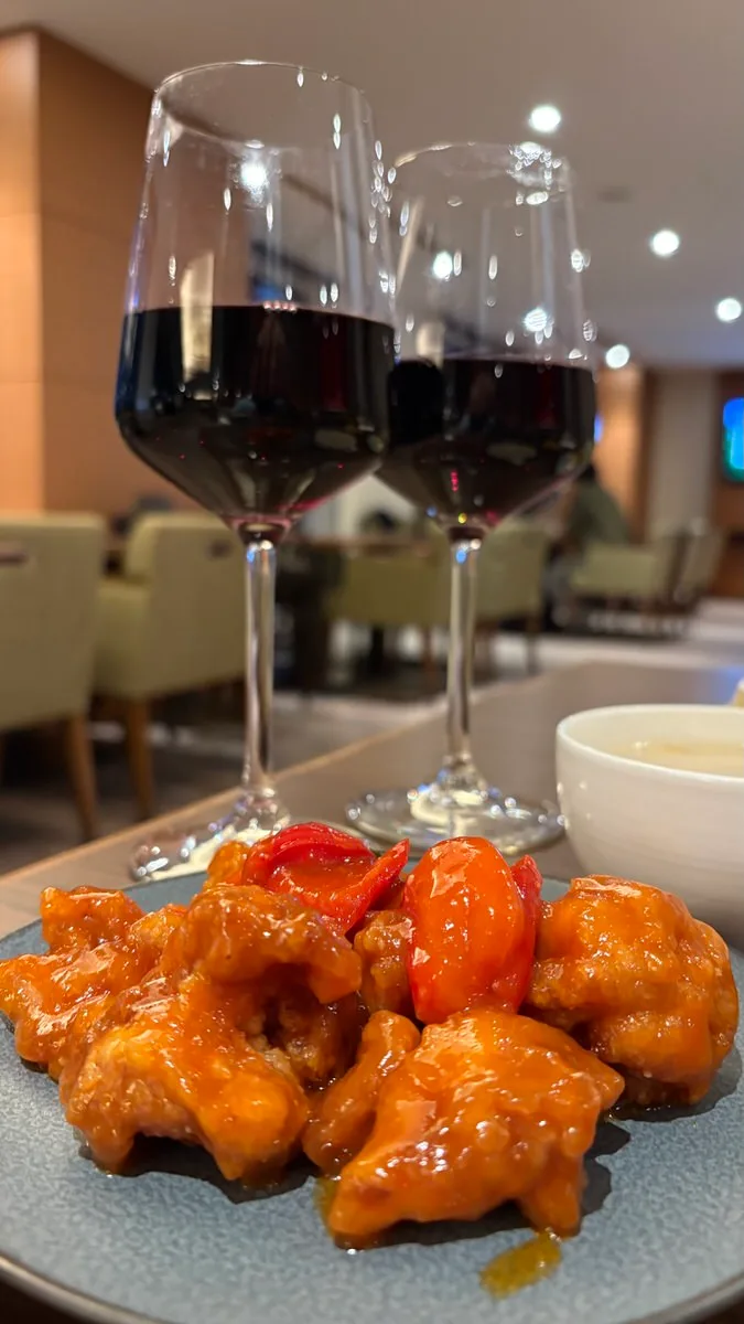 Two glasses of red wine behind a plate of fried chicken coated in chili sauce with pieces of tomato