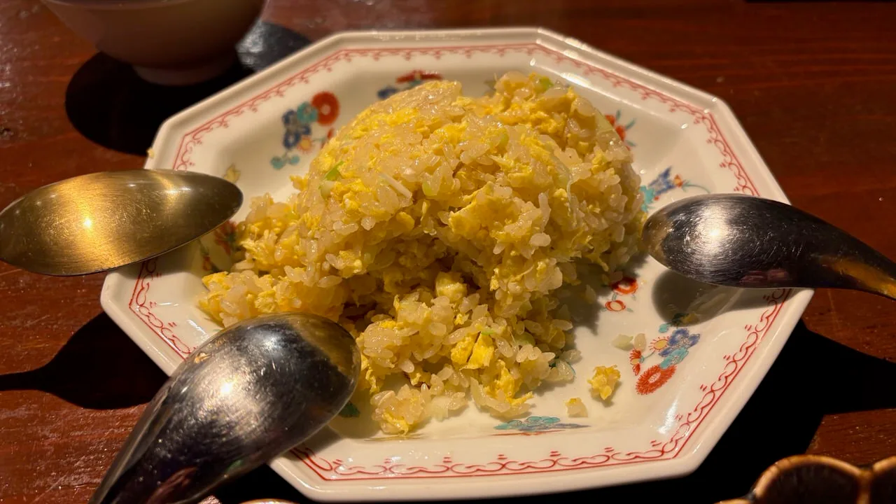 A plate of egg fried rice with spoons on a dark wooden table