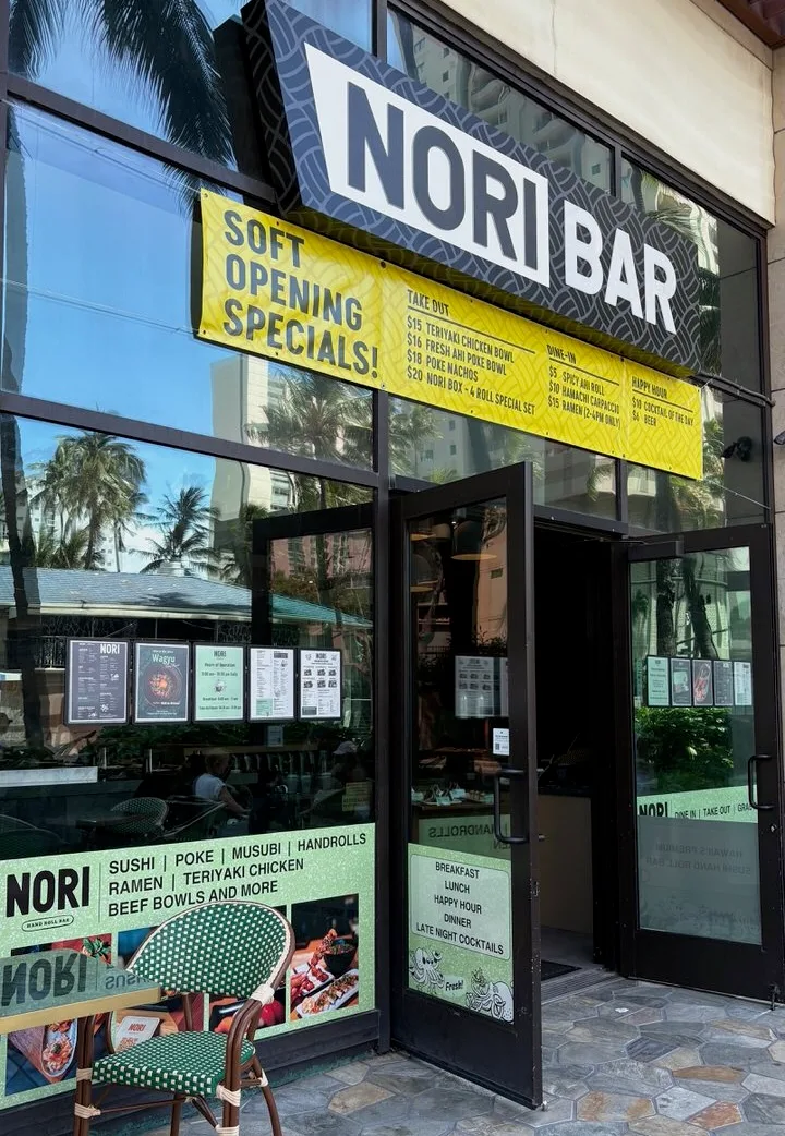 The Nori Bar storefront with a yellow Soft Opening Specials banner listing takeout, dine-in and happy hour prices, an open glass door, and a green-and-white bistro chair by the window