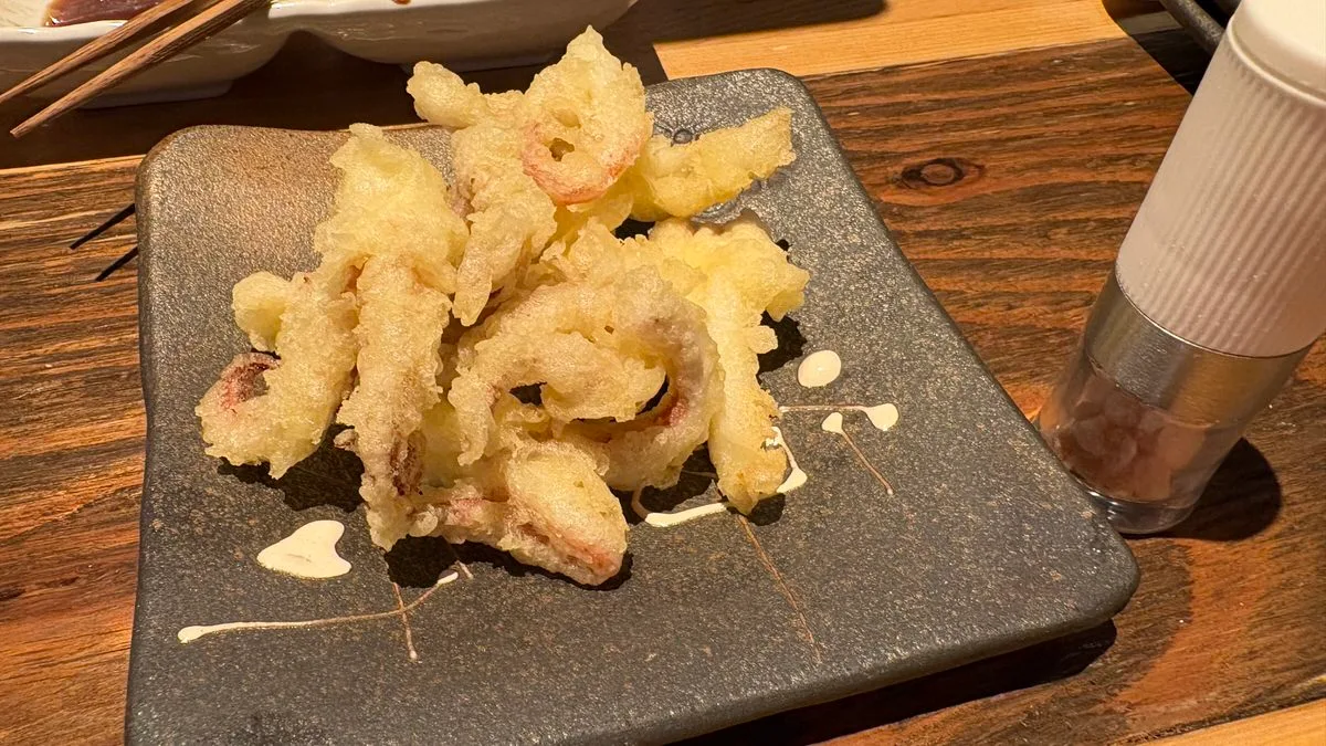 Fried squid tempura piled on a dark square plate, with lines of a mayonnaise-style sauce drizzled beside it