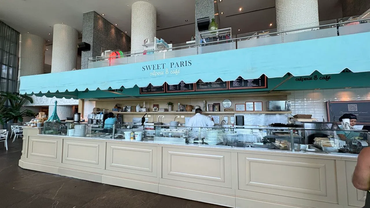 The Sweet Paris crêperie and café counter under a pale blue scalloped awning, menu boards above and staff working behind the glass