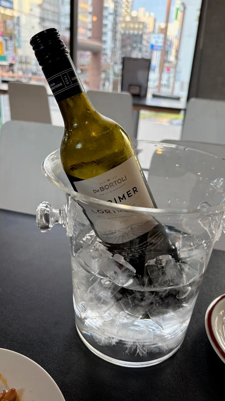 A bottle of De Bortoli Lorimer Shiraz Cabernet leaning in a clear glass bucket of ice and water on a dark table