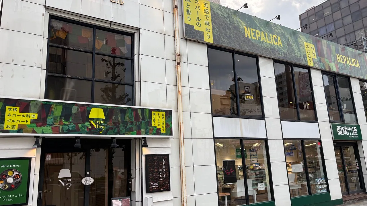 A white building with a green patterned awning over a street-level doorway and a large green banner reading NEPALICA across the second floor