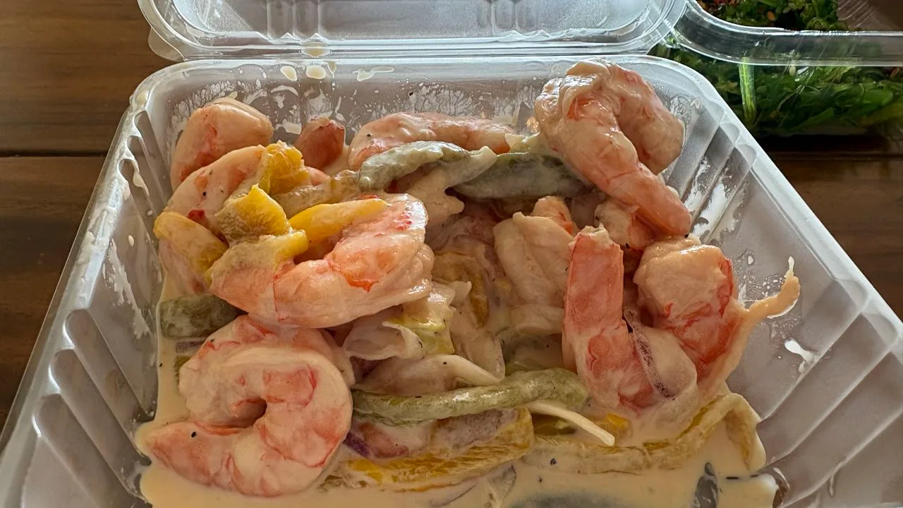A takeout box of shrimp in a creamy dressing with strips of pepper and onion