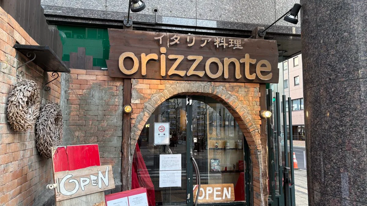A brick arch entrance under a wooden sign reading orizzonte, with two hand-painted OPEN signs beside the glass door