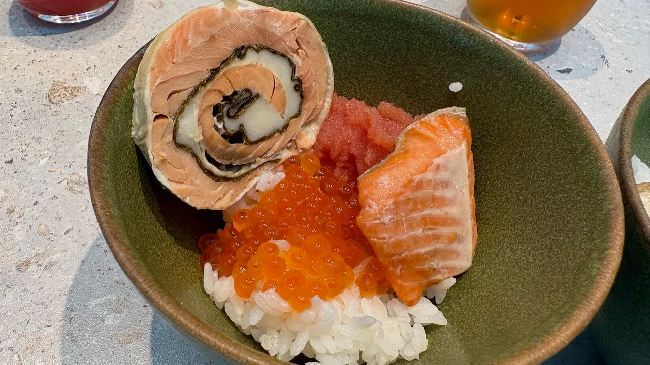 A green bowl of rice topped with salmon roe, a strip of tarako, a piece of salmon and a rolled salmon-and-yuba slice