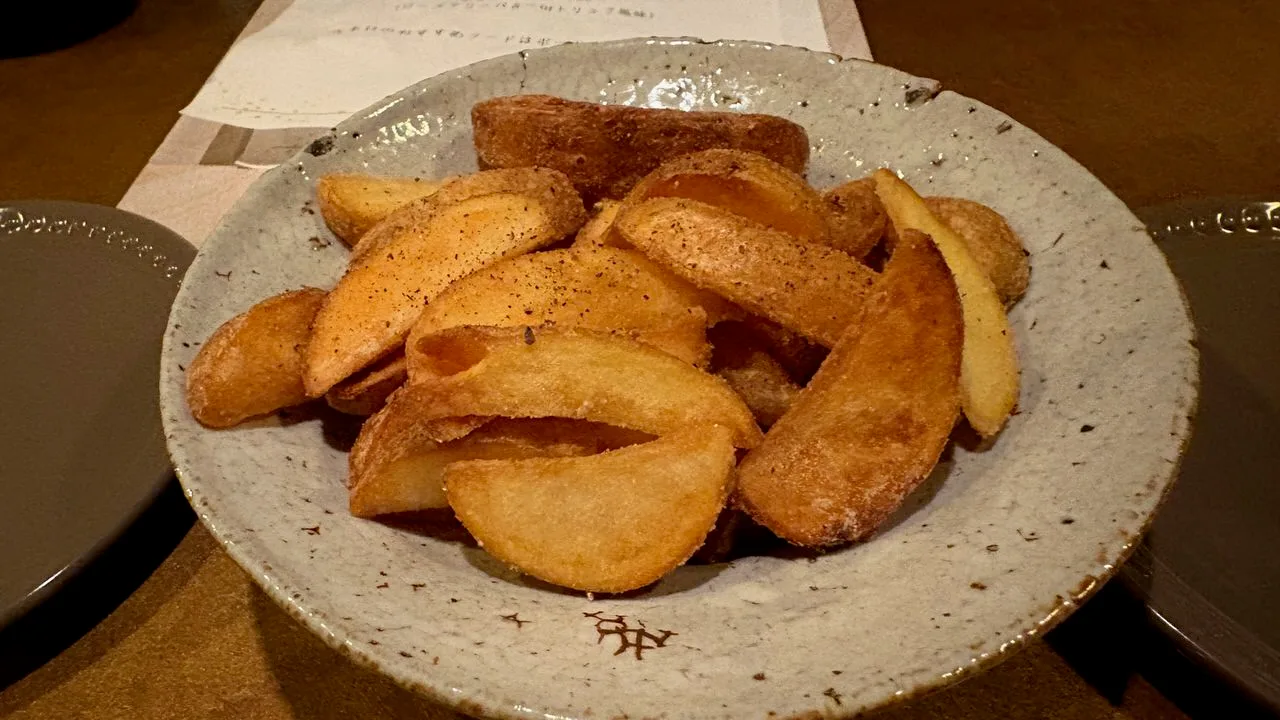 A pile of thick-cut fried potato wedges dusted with black pepper in a pale speckled bowl on a counter