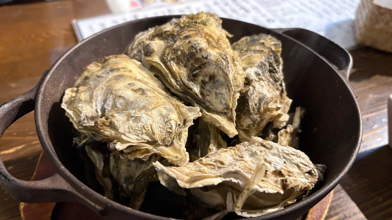 A black cast-iron pot packed with large steamed oysters in the shell on a wooden table