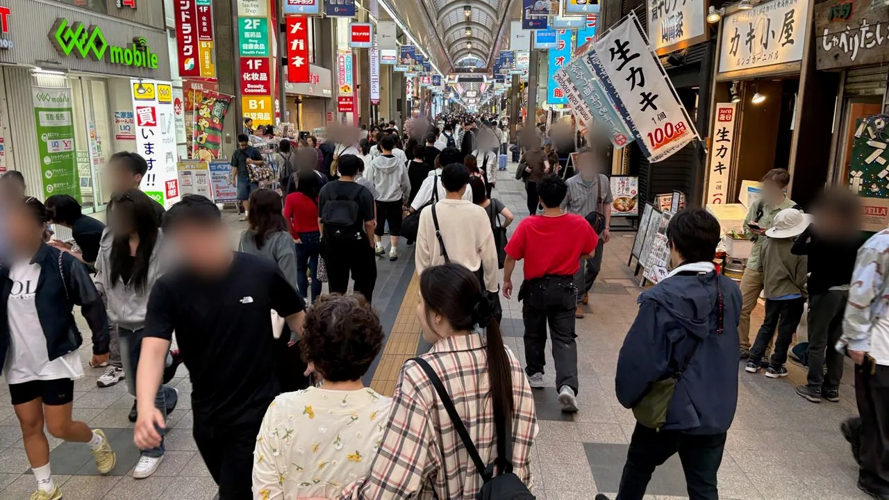 A covered shopping arcade in Sapporo full of people walking, with shop signs overhead and an oyster bar banner on the right