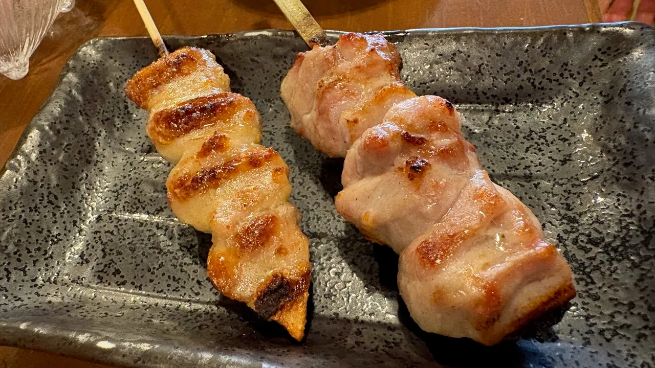 Two grilled skewers, chicken tail and chicken thigh, side by side on a speckled grey rectangular plate
