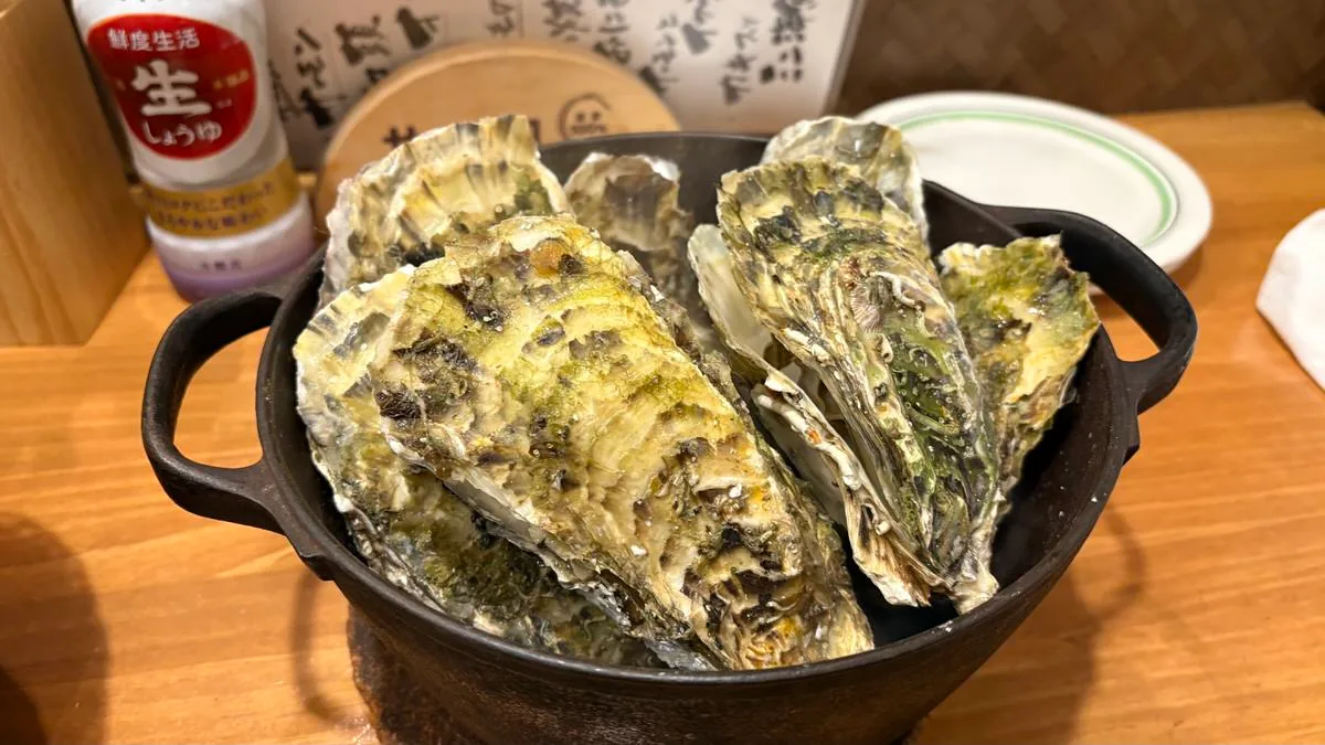 A black cast-iron pot filled with large steamed oysters in the shell on a wooden counter