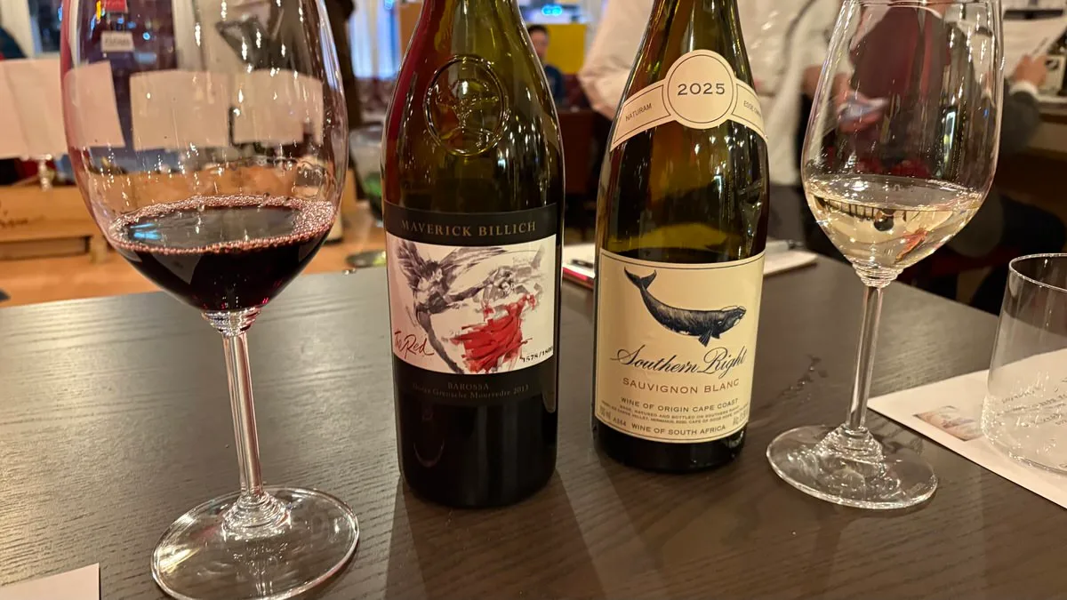 A glass of red wine and a glass of white wine on a dark table with two open bottles standing between them