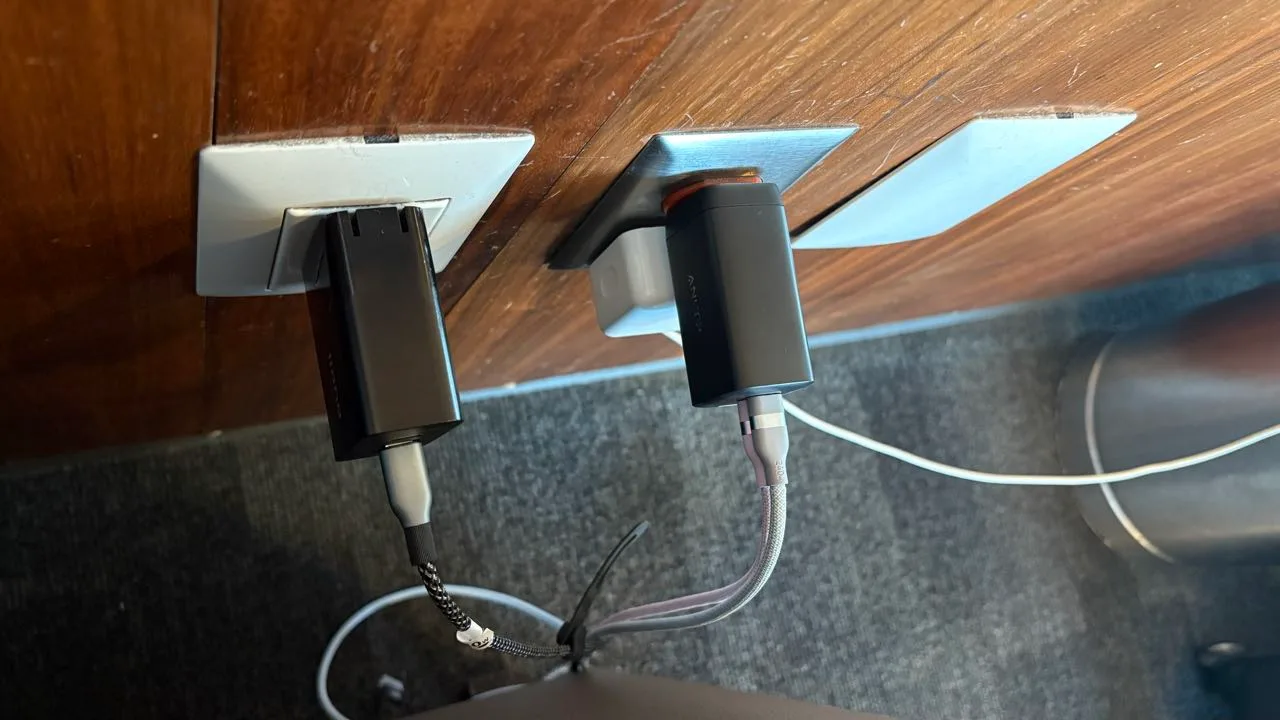 Two black USB power adapters hanging loosely out of wall sockets under a wooden panel, cables drooping to the carpet