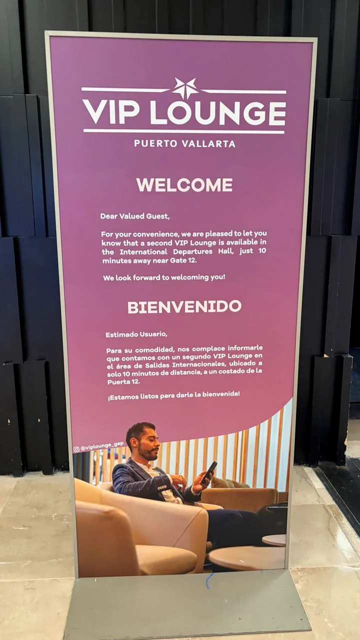 A tall purple standing sign reading VIP Lounge Puerto Vallarta, with a welcome message in English and Spanish about a second VIP Lounge near Gate 12