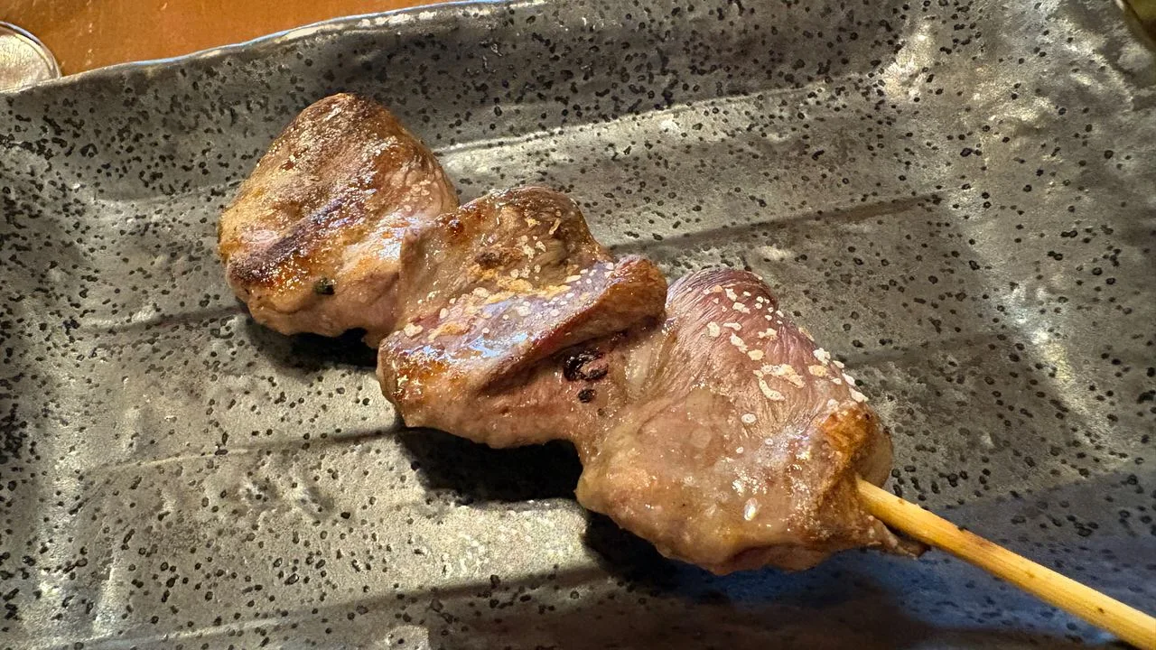 Three pieces of grilled chicken heart on a bamboo skewer, seasoned with salt, on a grey speckled plate