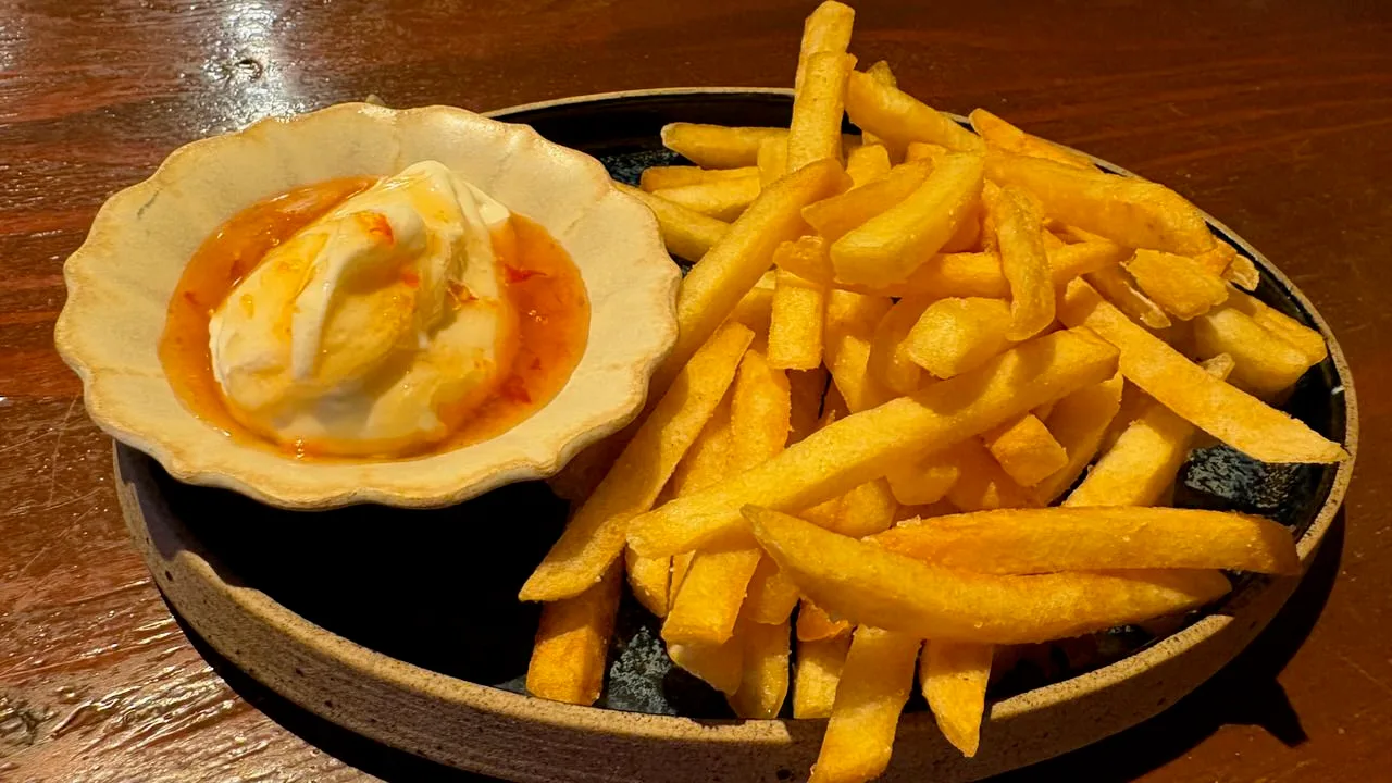 A plate of french fries next to a small dish of sour cream with orange sauce swirled through it